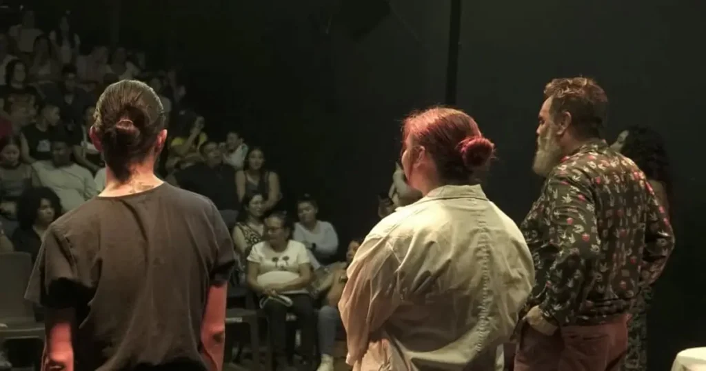 Actores de Ascetas conversan frente al público durante una presentación teatral