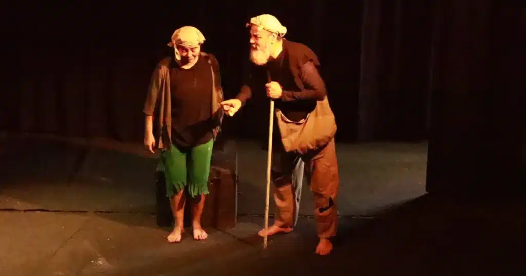 Dos actores de Ascetas realizan una escena teatral sobre un escenario con iluminación tenue