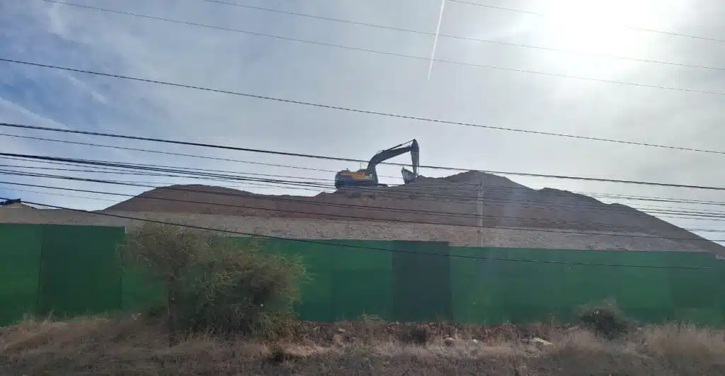 Excavadora trabaja sobre un gran acopio de tierra detrás del cierre verde de las obras del Hospital de Illapel.